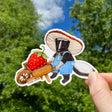 Skunk with Wheelbarrow & Strawberry Sticker showing a skunk in overalls with a large strawberry in a wheelbarrow outdoors.