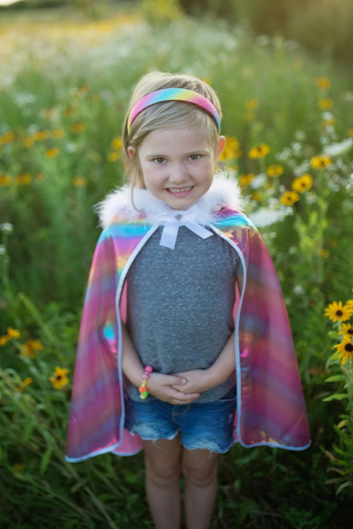 Young girl outdoors wearing the Rainbow Princess Cape with fluffy feather trim and sparkly silver edge closure.