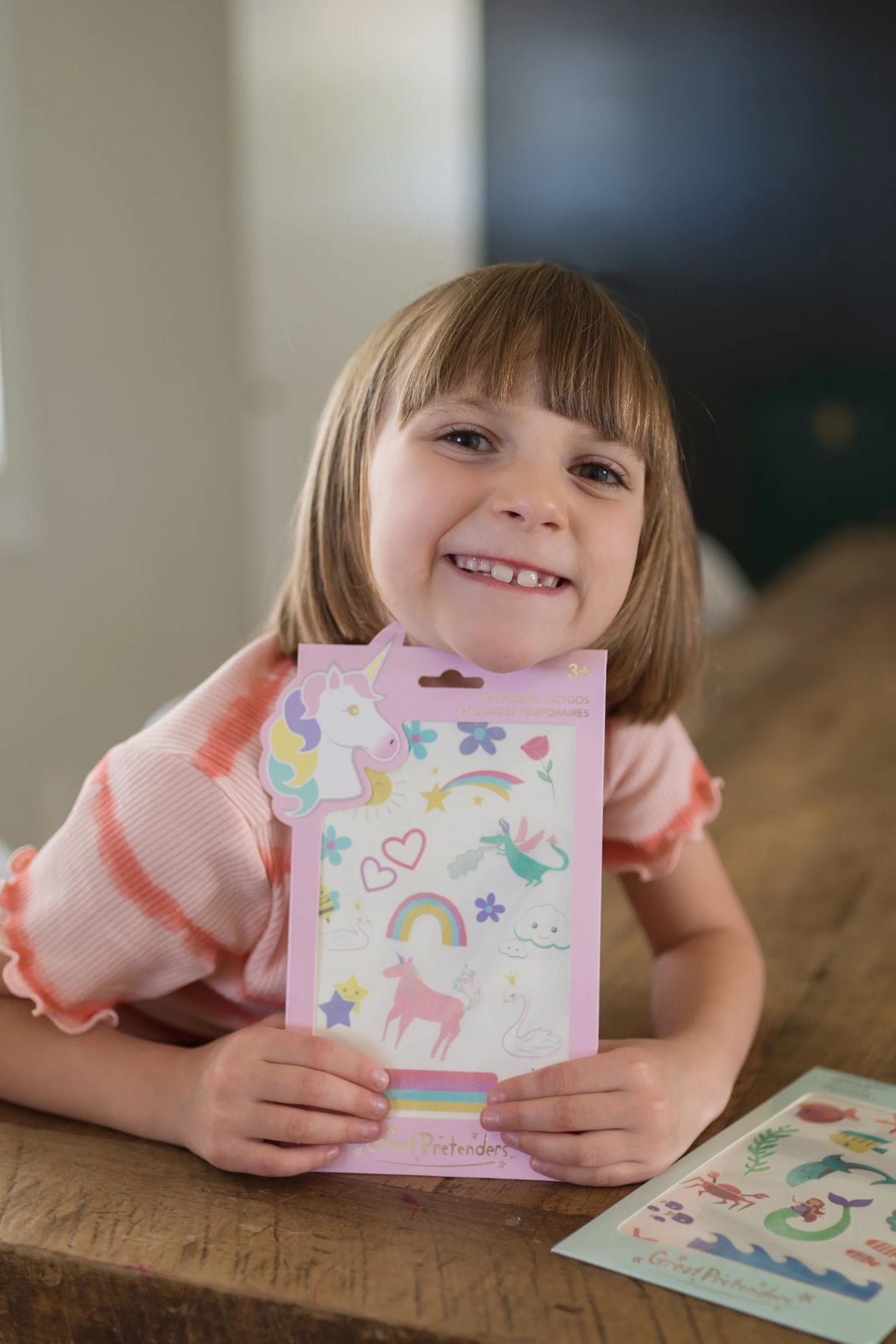 Smiling child holding Unicorn Tattoos set with rainbows, unicorns, and glittery magical temporary tattoos for kids ages 3+.