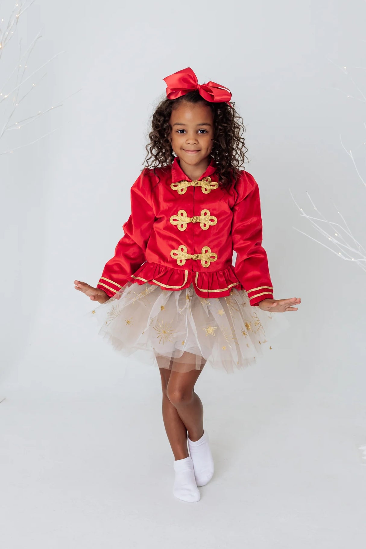 Girl wearing Sparkle Star Tutu size 4-6 with white tulle and shimmery gold star designs posing in red jacket.