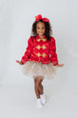 Girl wearing Sparkle Star Tutu size 4-6 with white tulle and shimmery gold star designs posing in red jacket.