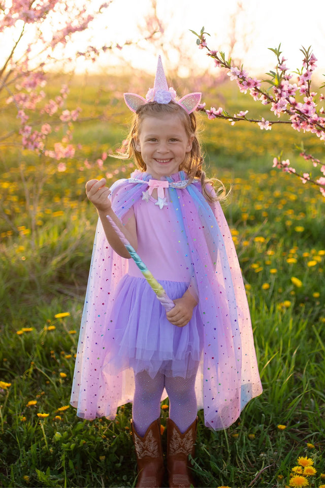 Young girl outdoors wearing Rainbow Unicorn Cape & Headband set with pastel cape and sparkly iridescent headband.