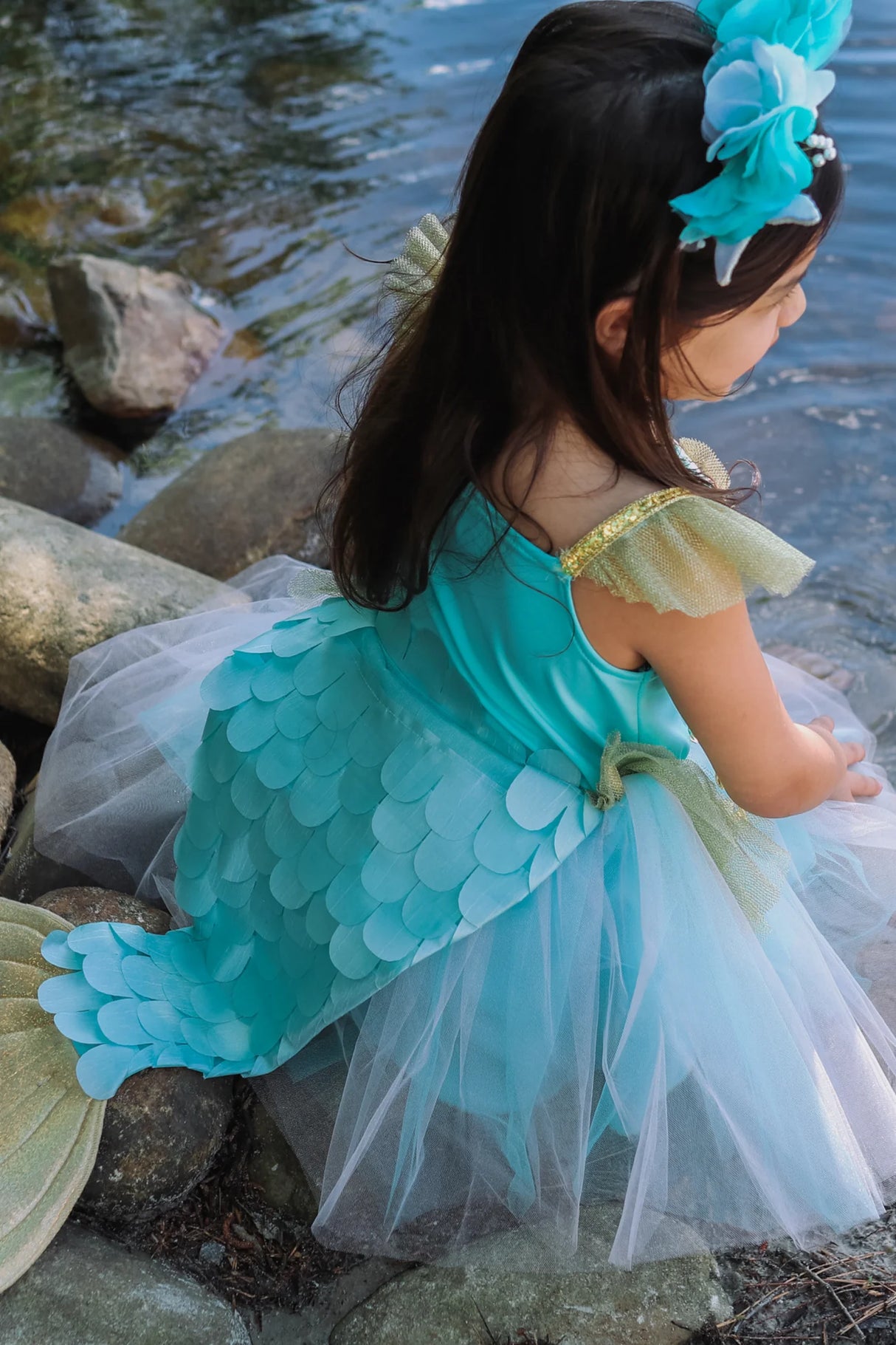 Child wearing a sea blue Mermalicious Dress with Tail featuring scalloped tail and tulle skirt by the water