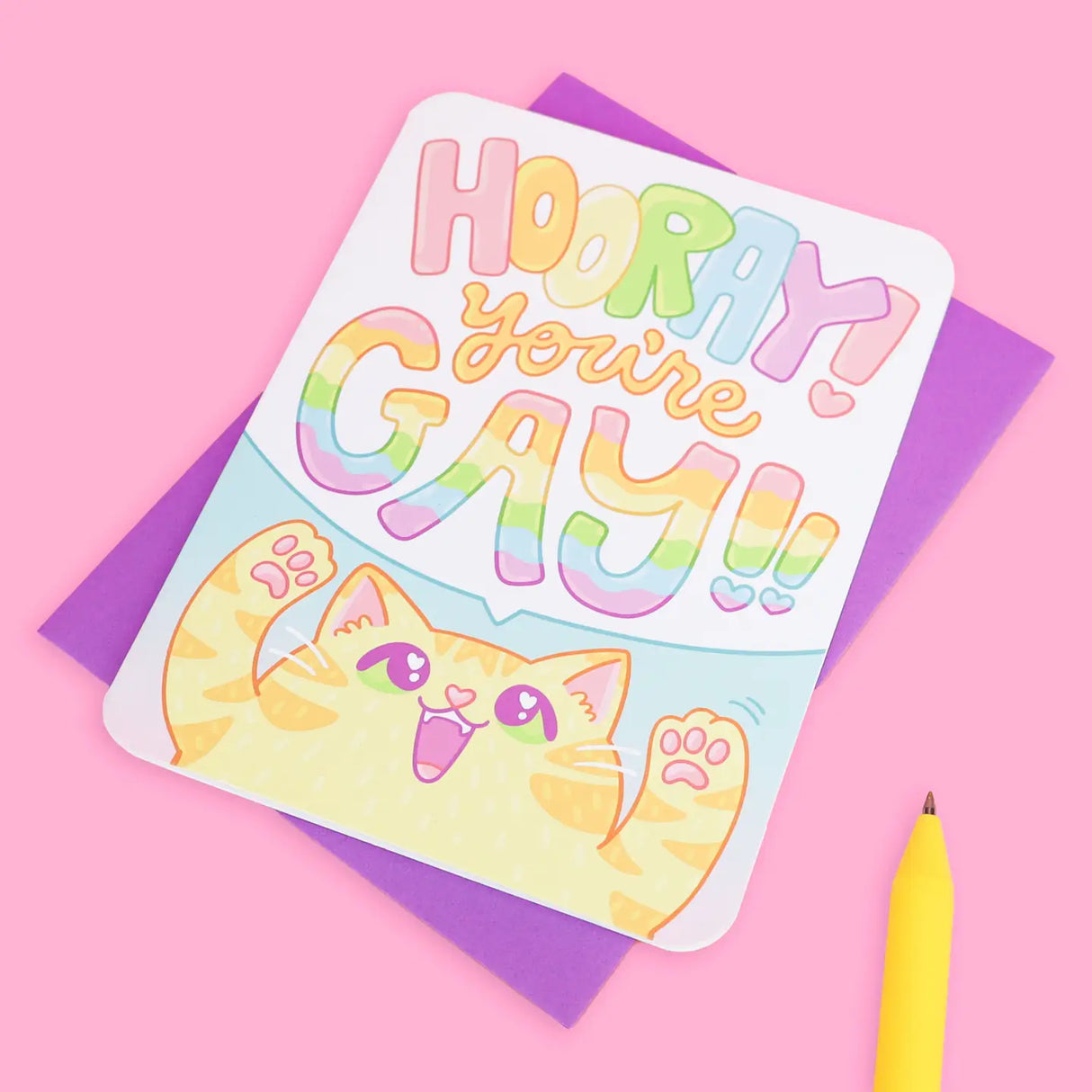 Hooray You're Gay! Card with a cheerful rainbow-colored text and cute cartoon cat on a purple envelope background