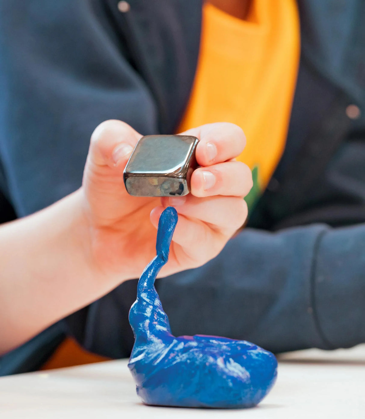 Hand holding magnet above iridescent blue Magnetic Storms Tidal Wave Thinking Putty creating magnetic effects.