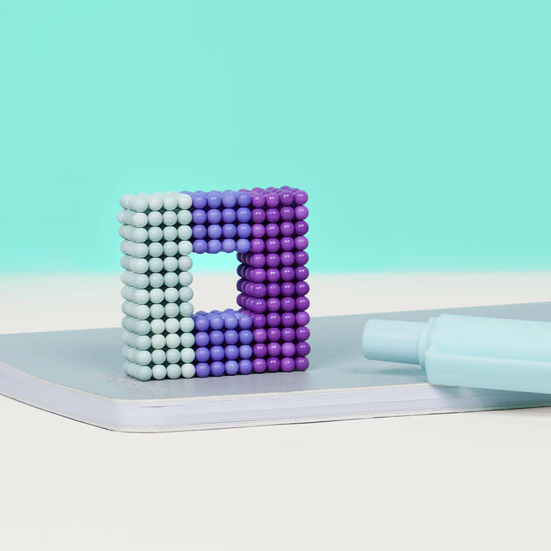 Speks. Bolds. Audacious magnetic balls shaped in a colorful square on a desk next to a pen.