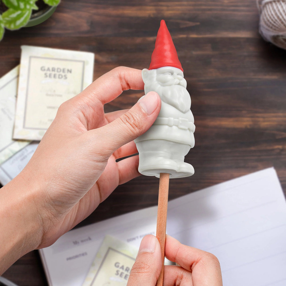 Hand holding Desk Gnome pencil sharpener and eraser with a red hat on a wooden desk background.