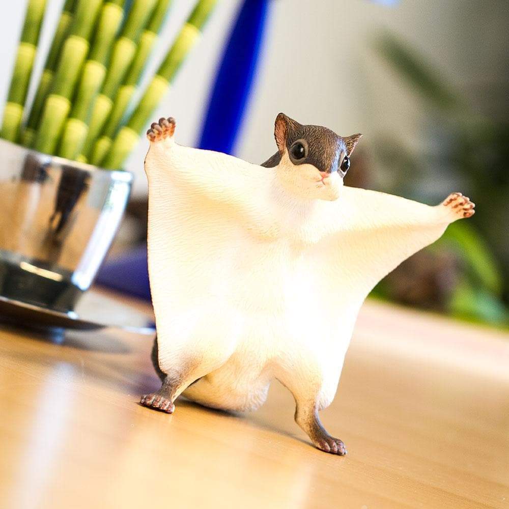 Flying Squirrel figurine with outstretched gliding membrane, lifelike and handcrafted, standing on a wooden surface.