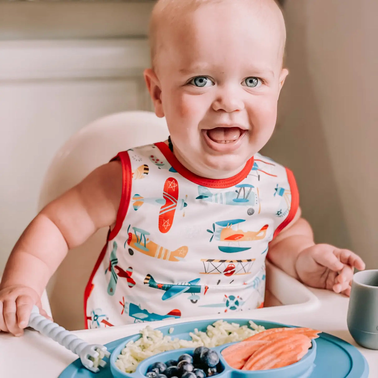 Baby wearing Bapron | Retro Airplanes 6M-3T bib-apron hybrid with colorful airplane print at mealtime.