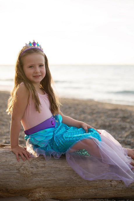 Mermaid Glimmer Skirt Set with Headband Lilac worn by girl sitting on driftwood at beach sunset.