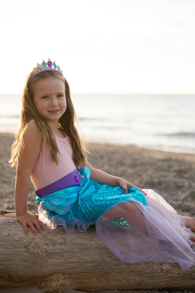Mermaid Glimmer Skirt Set with Headband Lilac worn by girl sitting on driftwood at beach sunset.