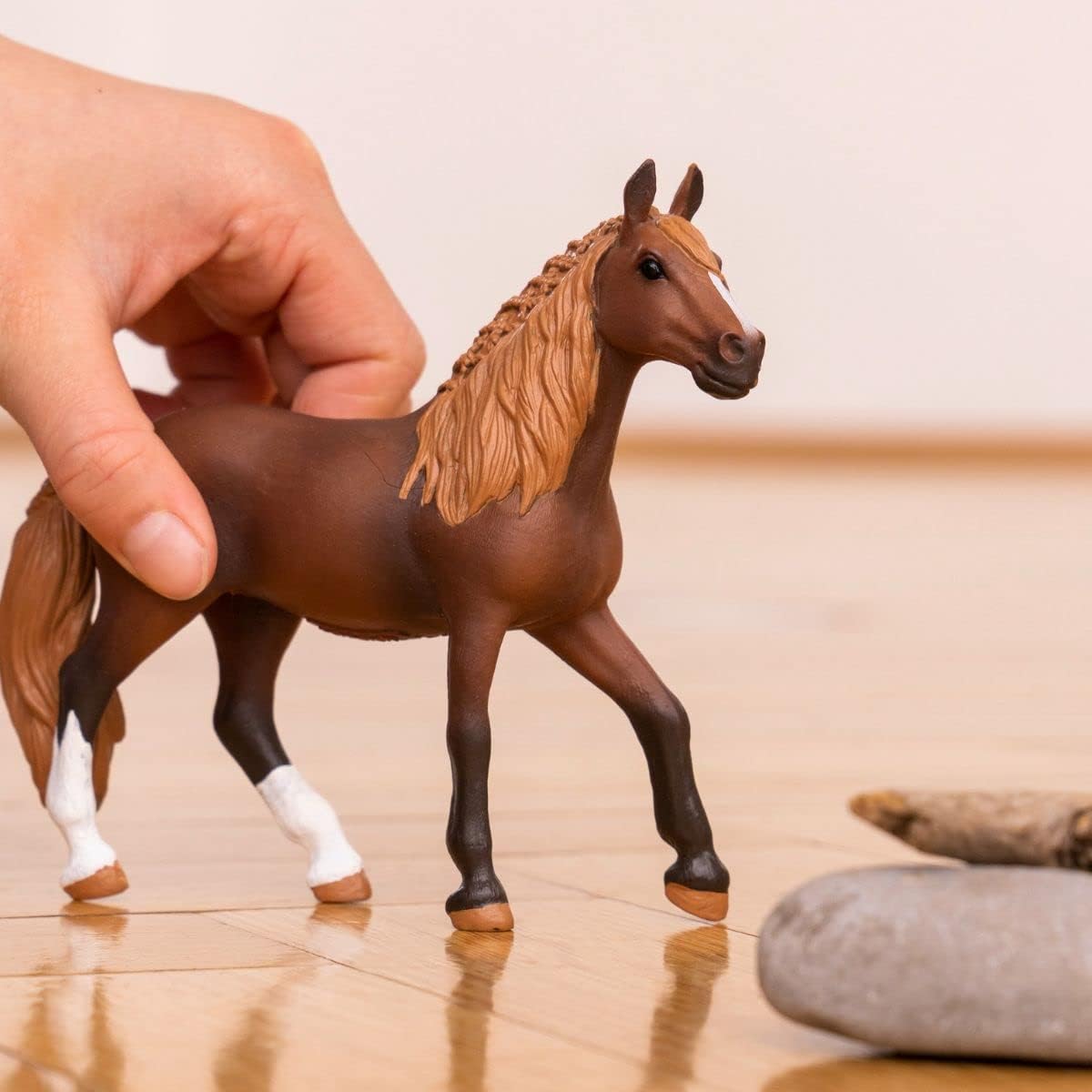 Peruvian Paso Mare Horse toy with braided mane and flowing tail held by a hand on a wooden floor.