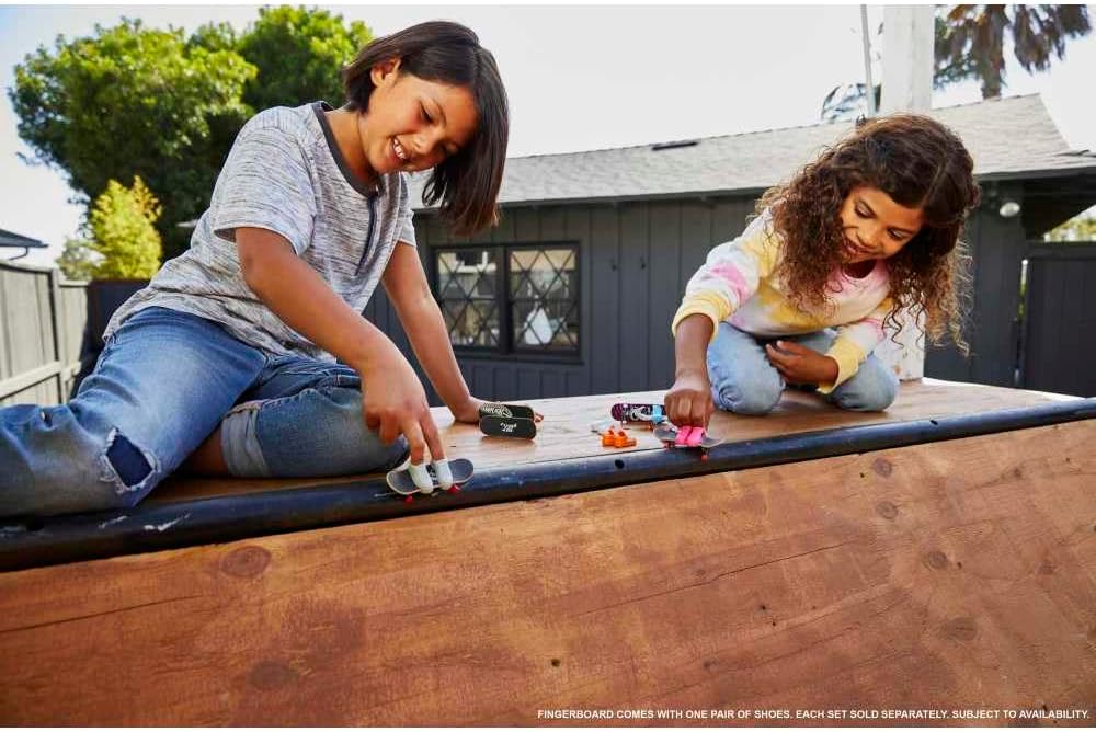 Children playing with Hot Wheels Skateboard & Shoes mini skateboards and shoes on a wooden ramp outdoors.