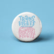 Button | Trans Rights Are Human Rights with blue and pink lettering on a white 1.25-inch round pin for self-expression