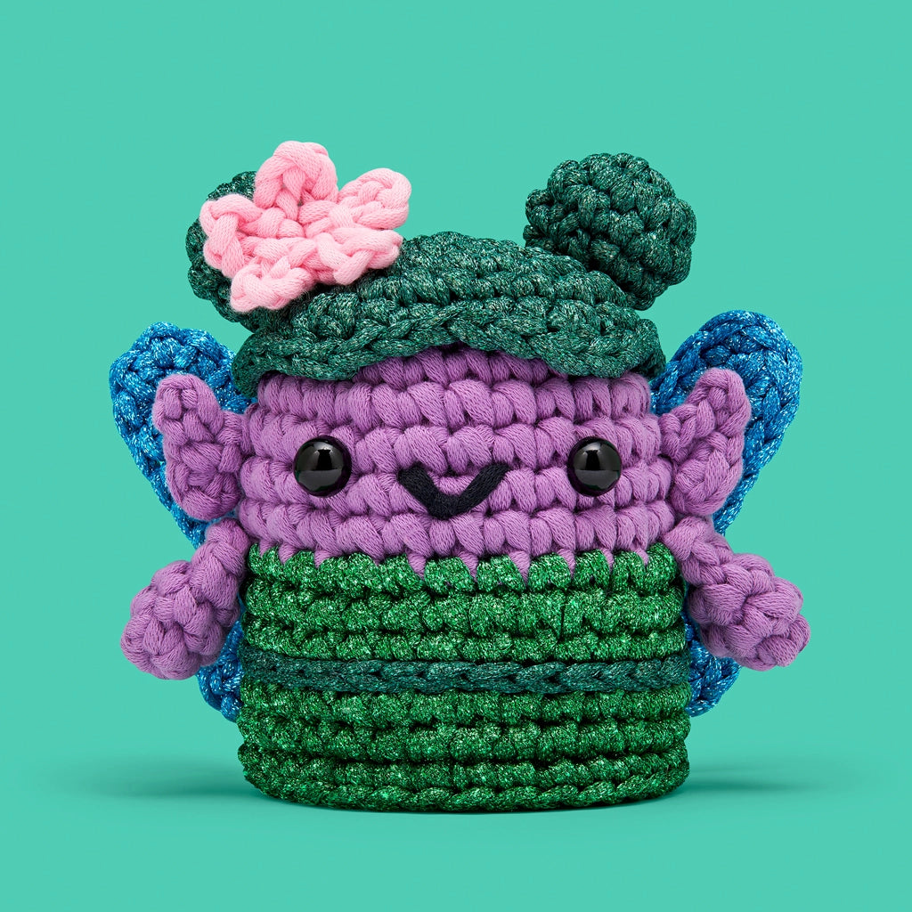 The Woobles Crochet Kit | Esperanza the Fairy purple crochet fairy with green hat and pink flower on teal background
