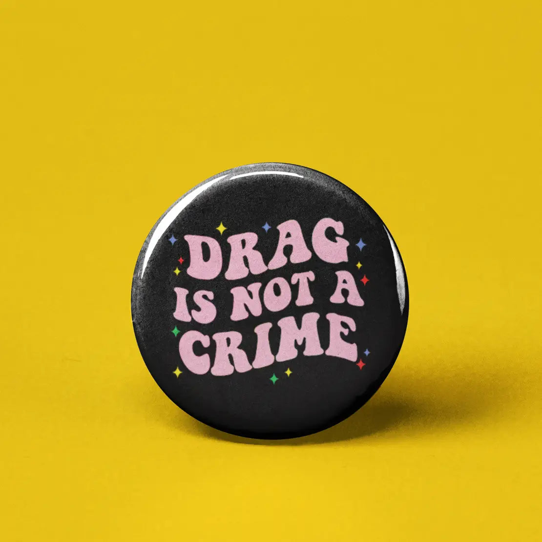 Button | Drag is Not a Crime round black 1.25-inch pin with pink text and colorful star accents on yellow background