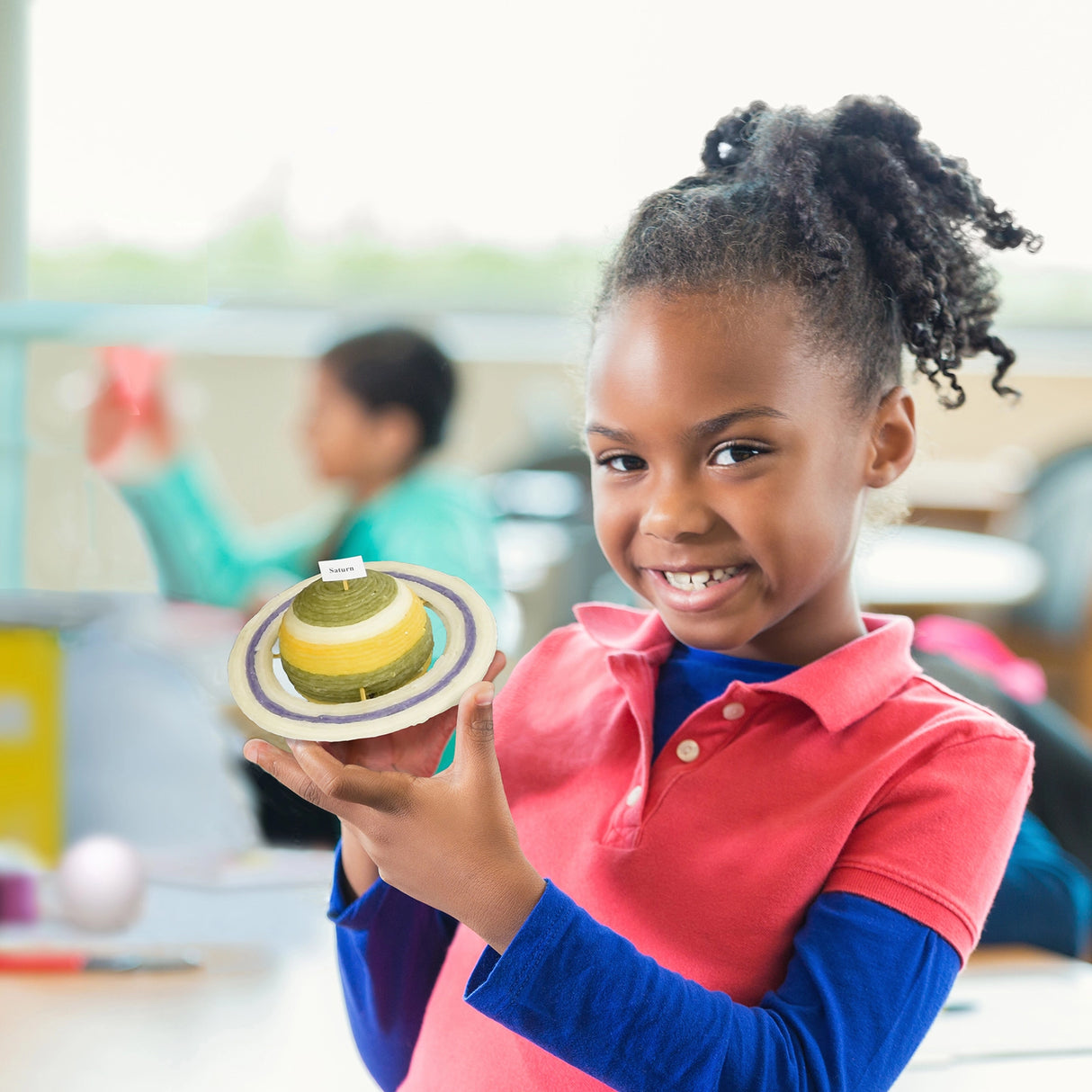 Young girl smiling and holding a solar system model made with Wikki Stix Nature Pack in a classroom setting.