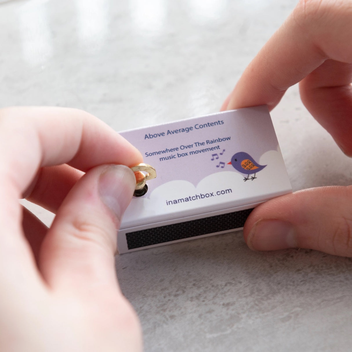 Hands winding the Somewhere Over the Rainbow Musicbox Matchbook playing the uplifting tune inside a matchbox.