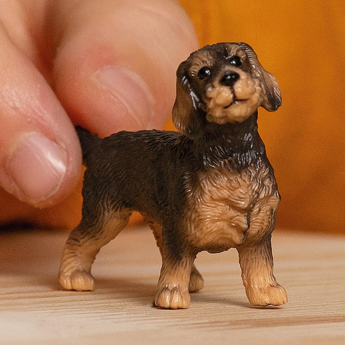 Wire-Haired Dachshund figurine with detailed fur and lifelike features, held by hand on a wooden surface.