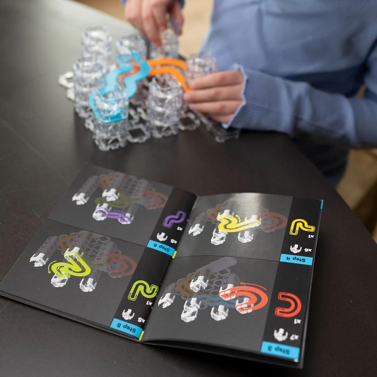 Trestle Tracks Deluxe Set showing hands assembling clear stacking cubes and connecting colorful track pieces.