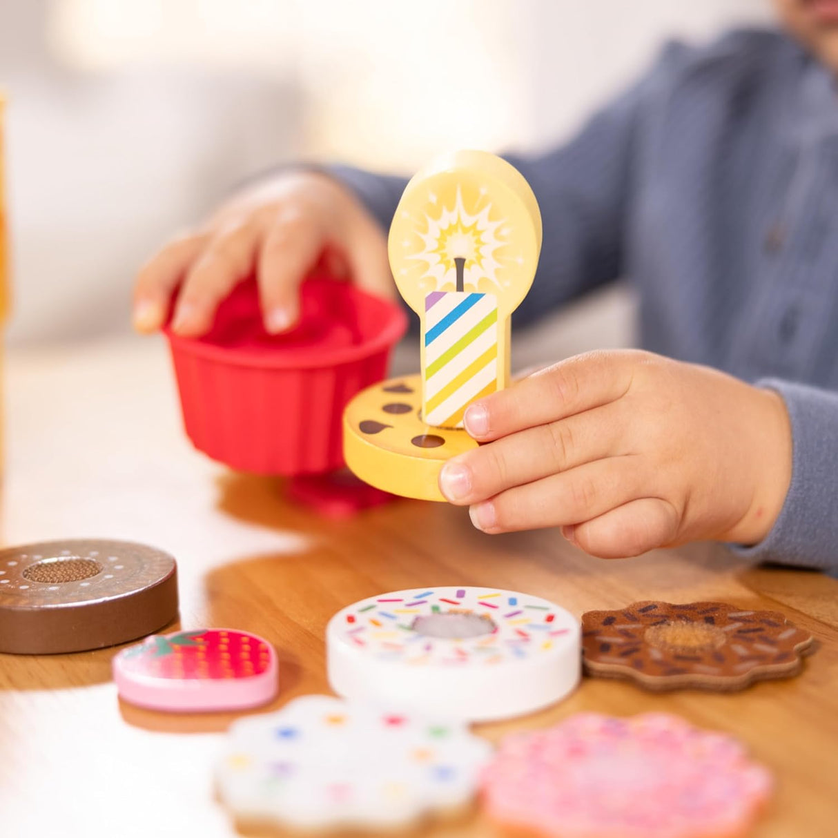 Child playing with colorful wooden play food from the Play to Go Cake & Cookies Play Set on table.