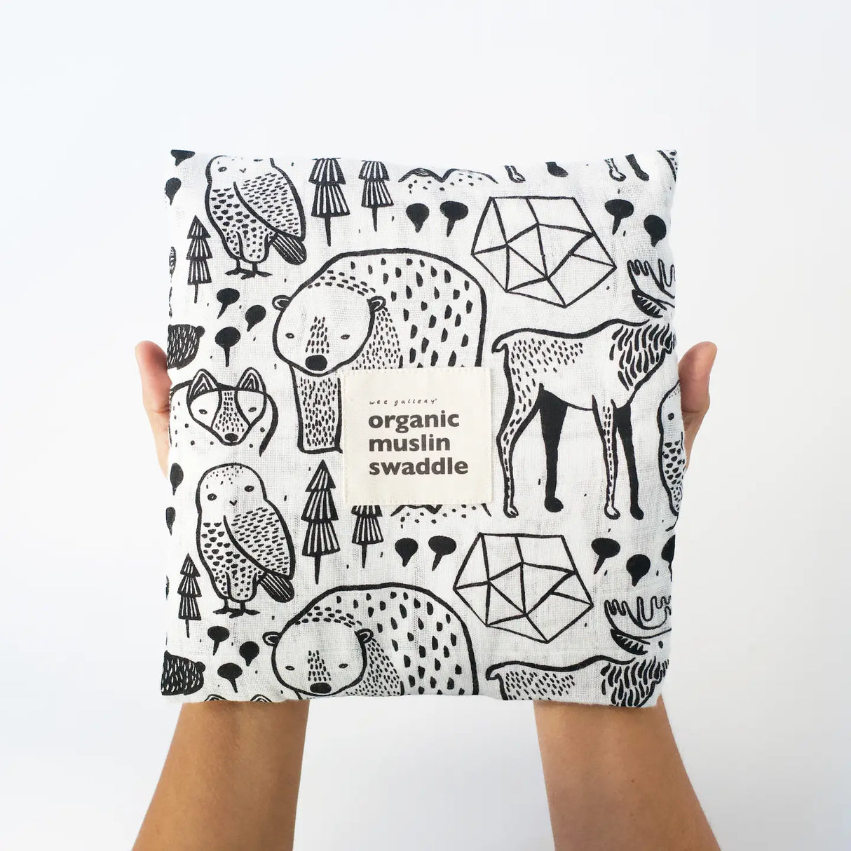 Hands holding Organic Muslin Swaddle | Nordic with black and white animal and forest patterns on soft fabric.