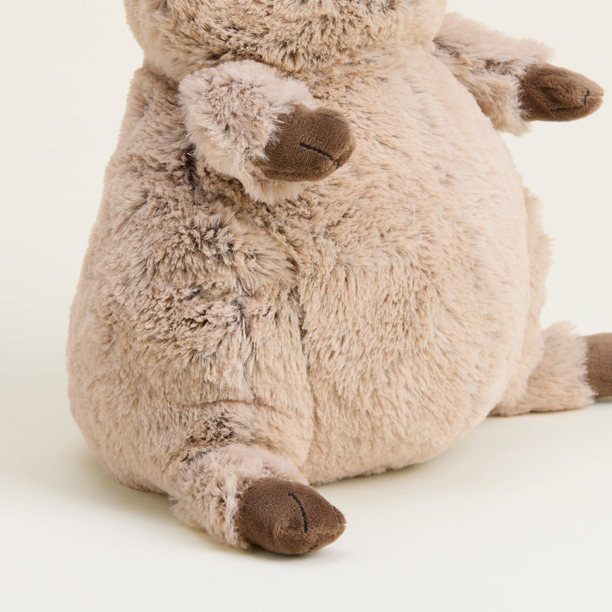 Close-up of a soft, plush quokka toy with beige fur and brown paw details sitting on a neutral background.