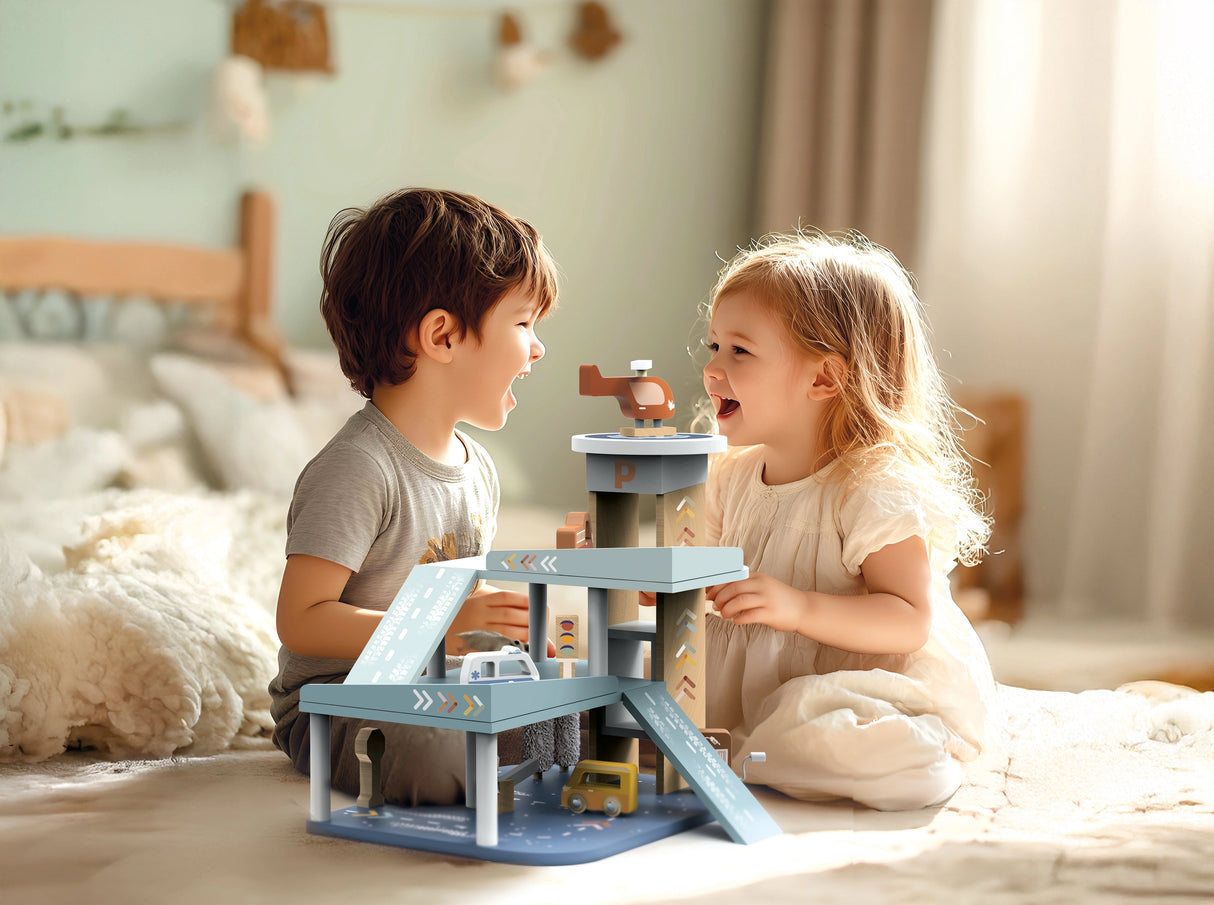 Two young children happily playing with a colorful wooden garage playset featuring cars and a helicopter indoors