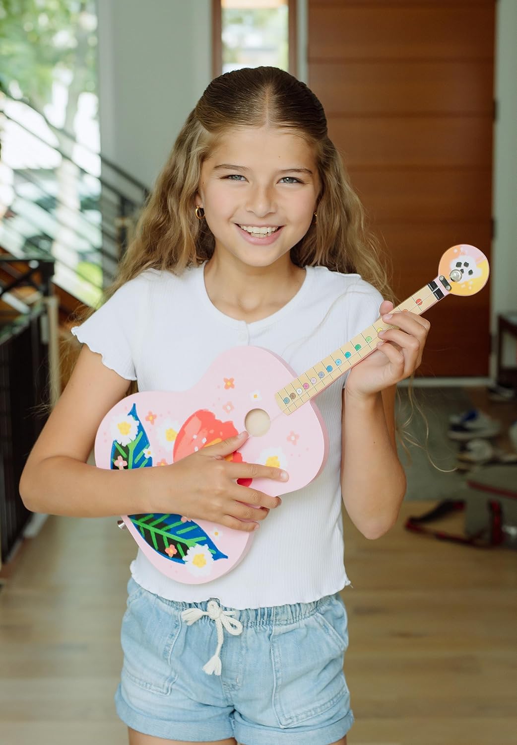 Smiling girl holding the TinkerTar Pink Floral Acoustic 1-string guitar designed for young beginners.