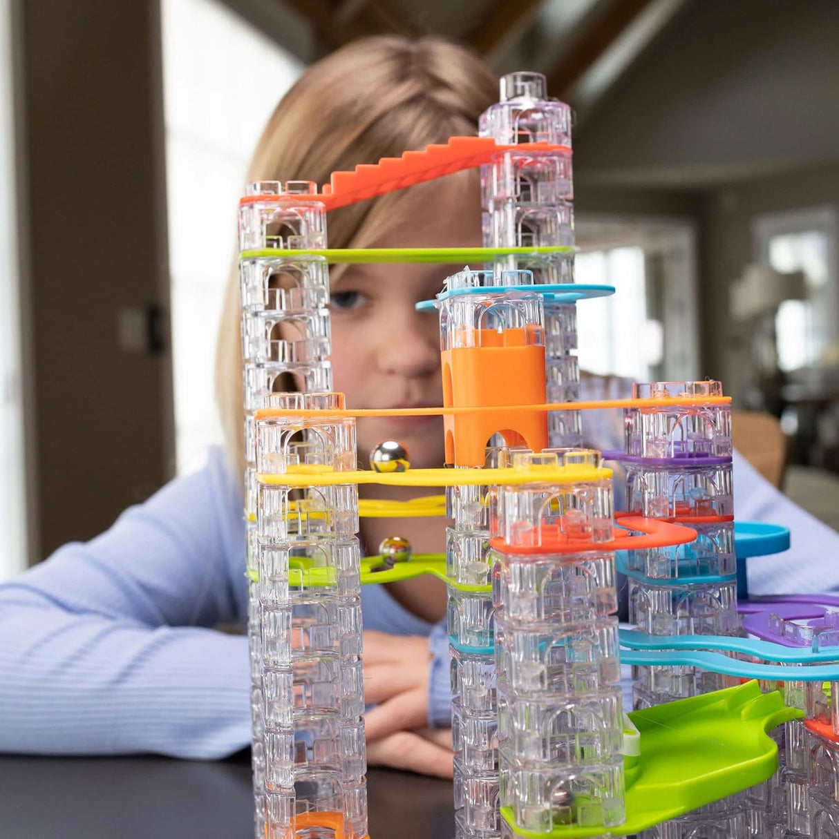 Child playing with colorful Trestle Tracks Deluxe Set with clear stacking cubes and marbles on a table indoors.