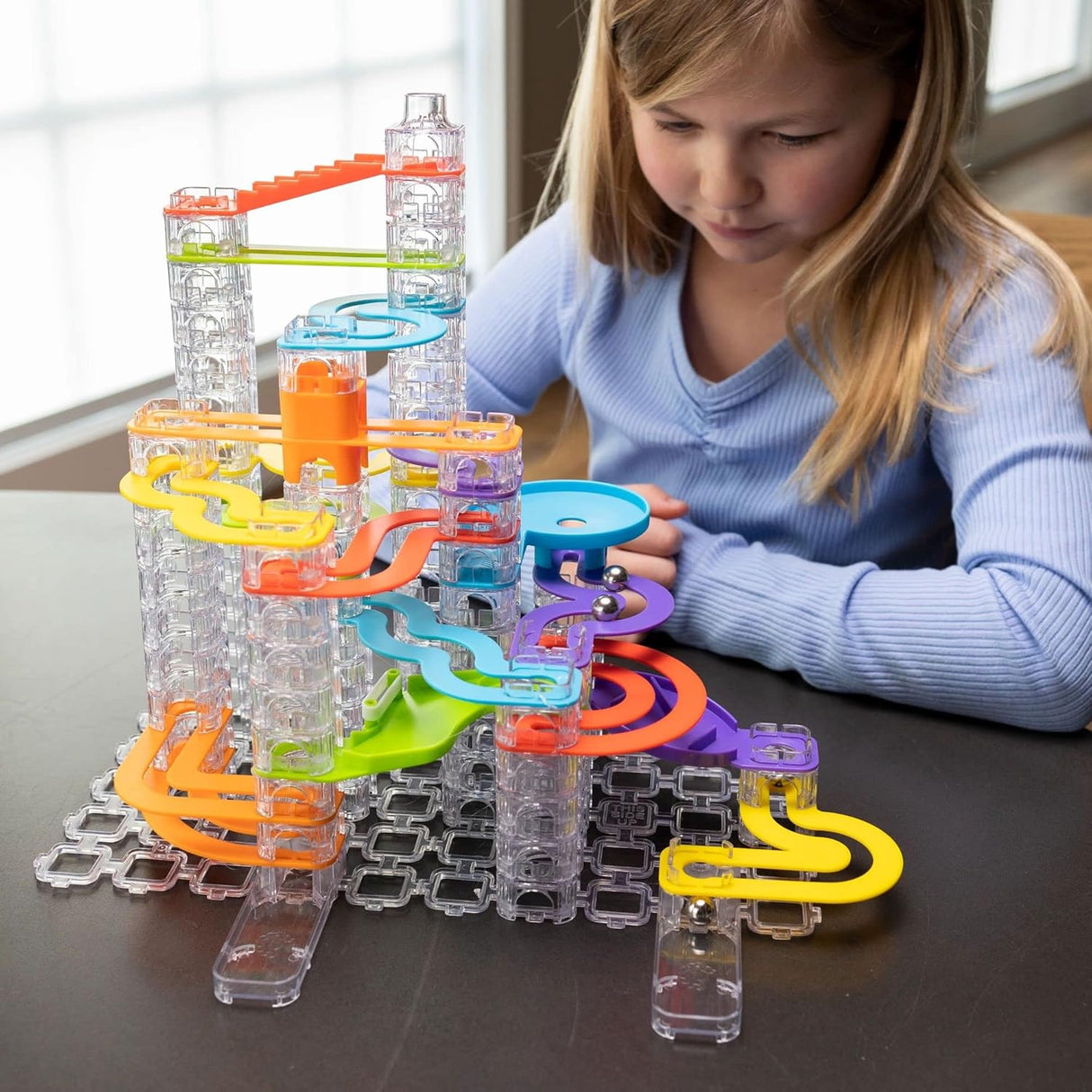 A child playing with colorful Trestle Tracks Deluxe Set featuring clear stacking cubes and winding marble tracks.