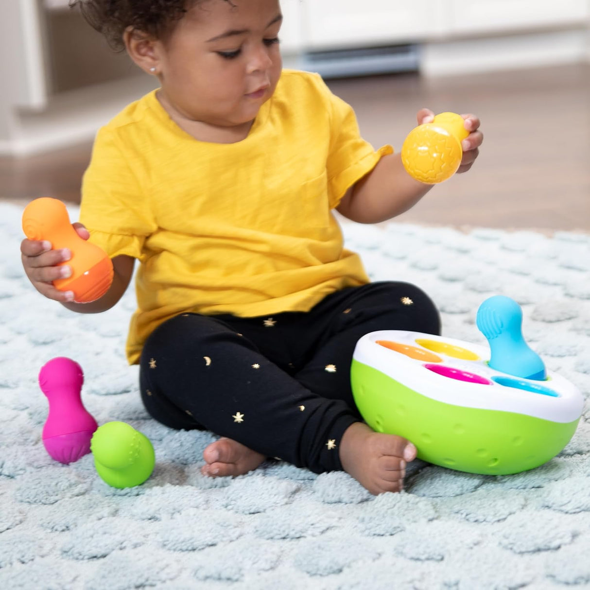 Toddler playing with colorful textured SpinnyPins and wobble bowl on soft rug for sensory play.