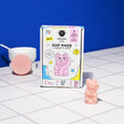 DIY Soap Maker Kitty box with pink cat-shaped soap and soap bar on white tiled surface against blue background.