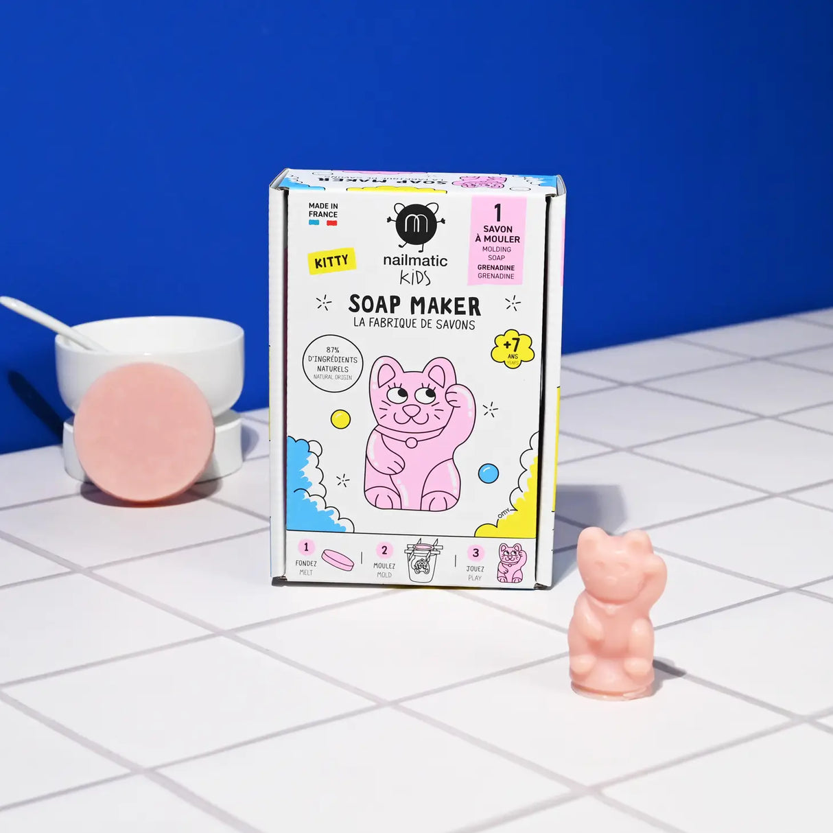 DIY Soap Maker Kitty box with pink cat-shaped soap and soap bar on white tiled surface against blue background.