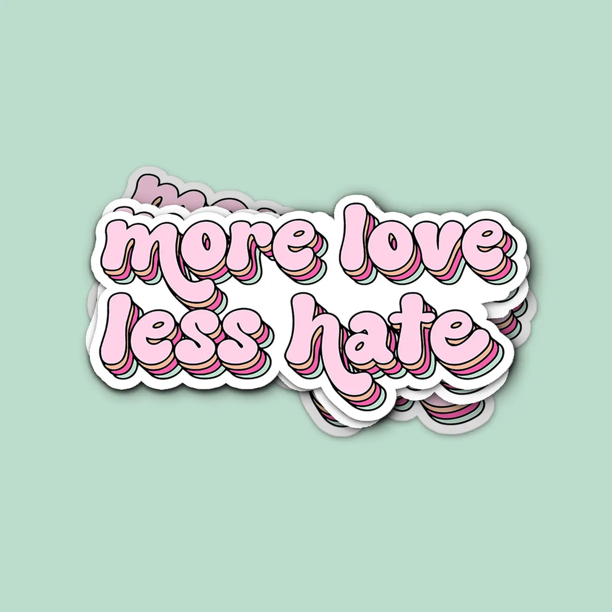 Stack of More Love Less Hate Sticker with pink retro text on a matte vinyl finish against a green background.