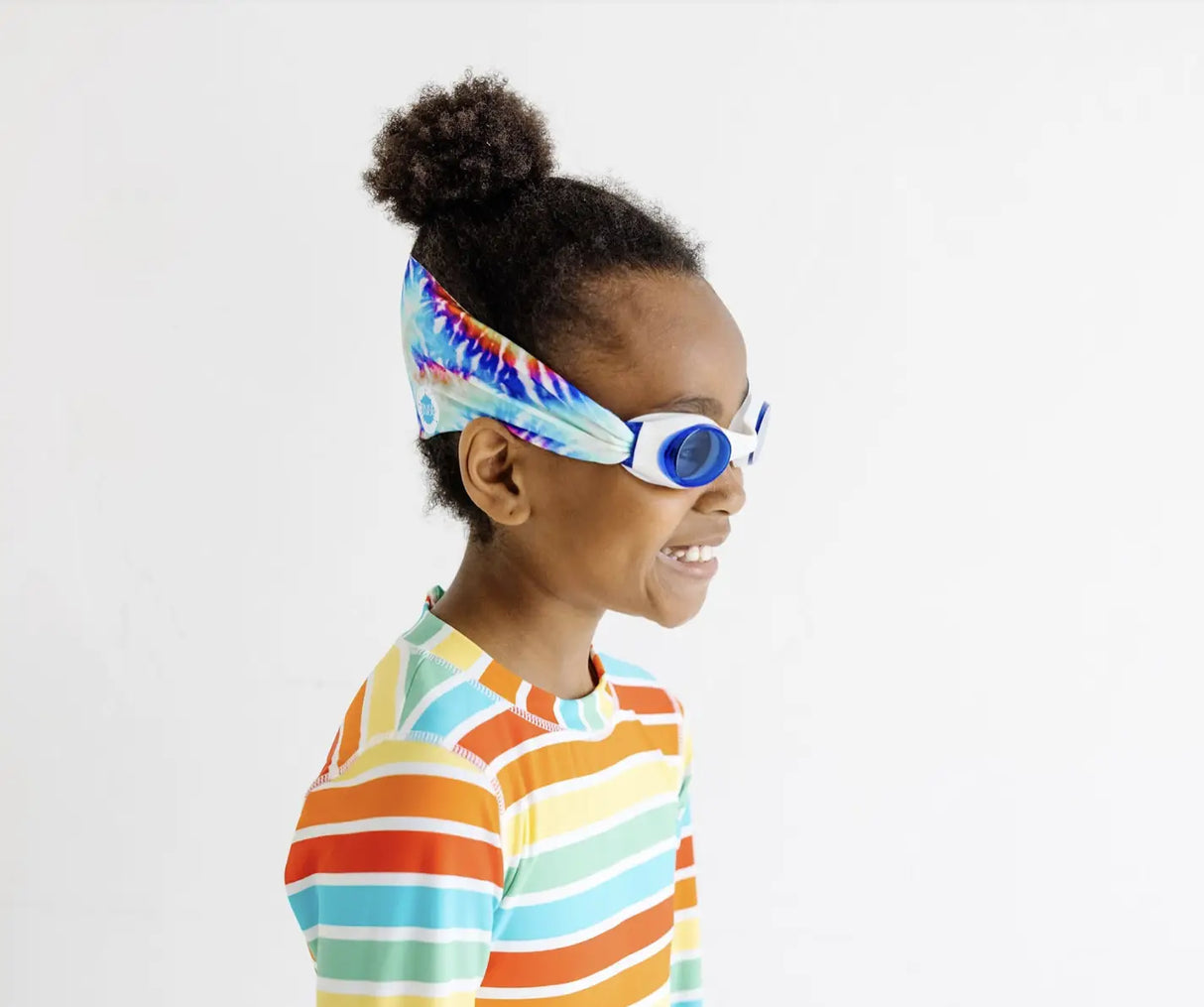 Child wearing Goggles Tie Dye with tangle-free strap and tinted blue lenses smiling in colorful striped shirt
