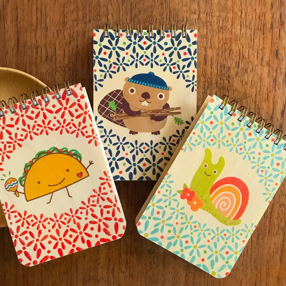 Mini Wood Notebook | Snail with colorful snail, taco, and beaver cartoon covers on a wooden table.