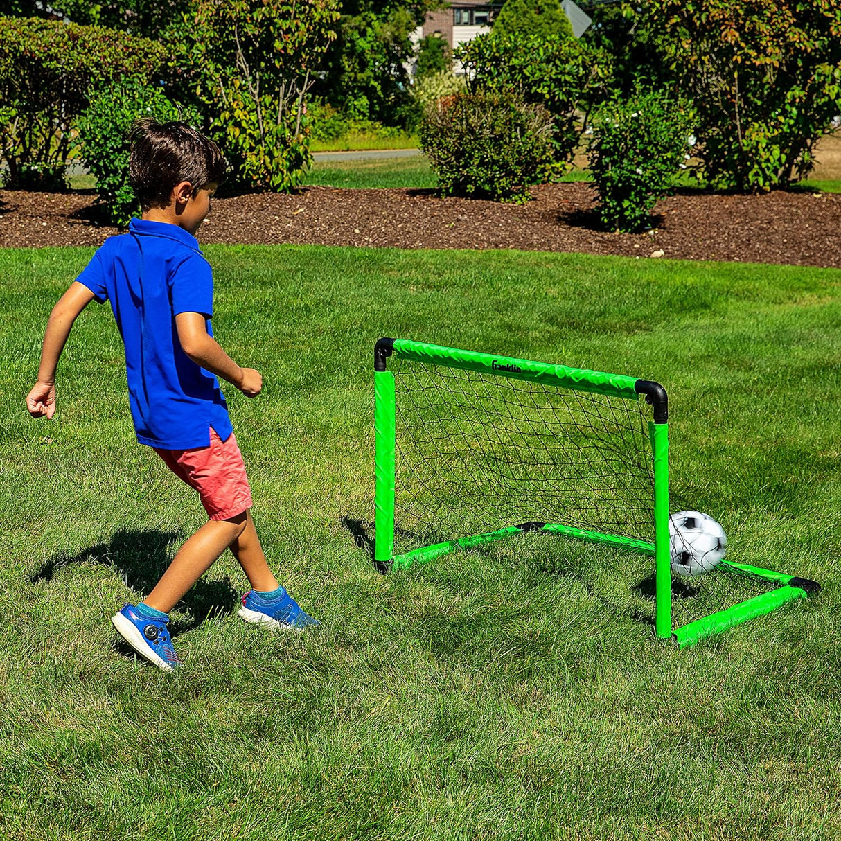 Child playing soccer with a bright green Soccer Goal with Ball & Pump set on grass outdoors.