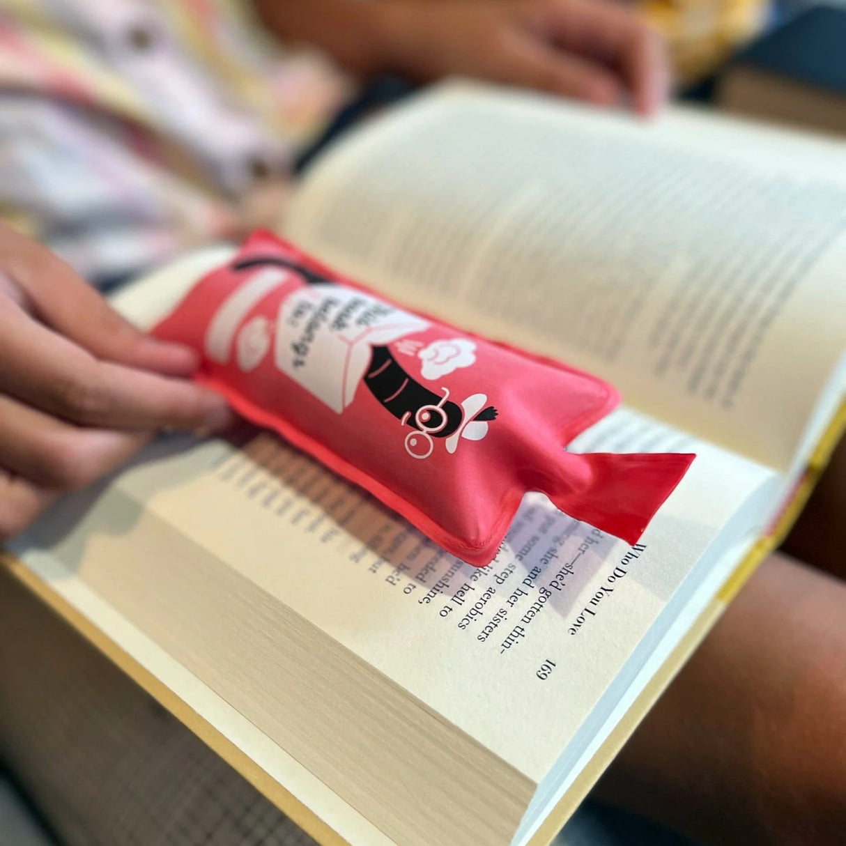 Bookie Cushion Bookmark placed in an open book, showing a fun and practical fart gag bookmark.