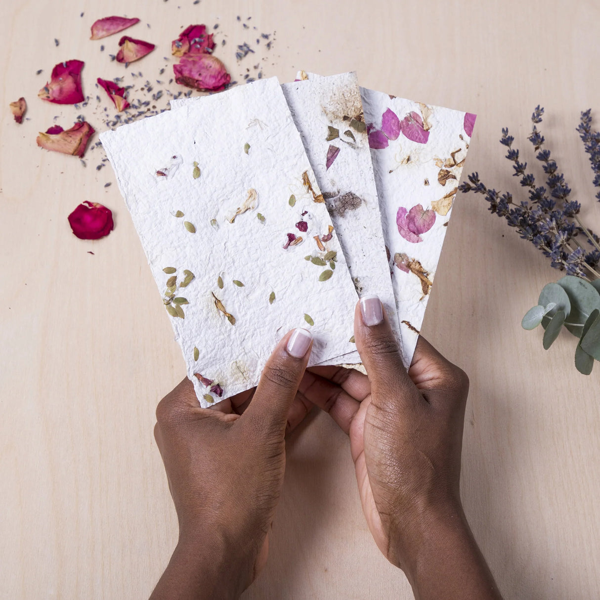Hands holding three unique flower paper sheets made with the Crafters Flower Paper Kit.