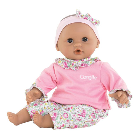 12-inch baby doll with brown eyes wearing pink pajamas and a floral headband sitting and smiling gently
