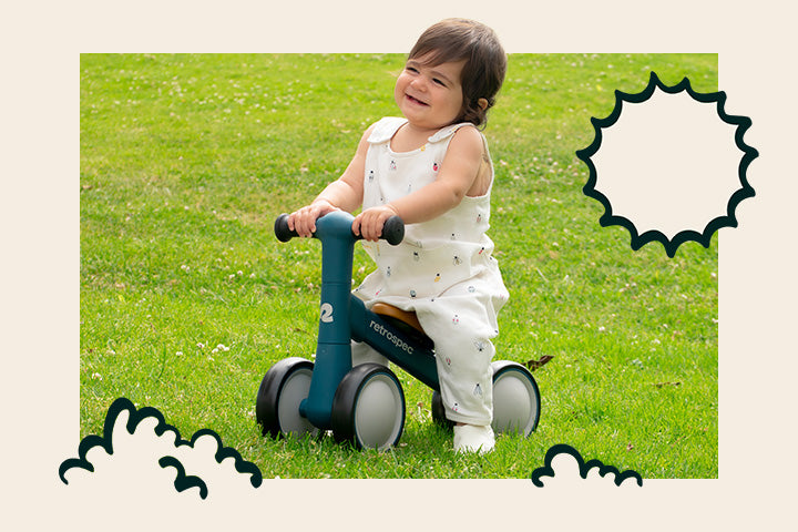 Child riding a blue Cricket 2 Baby Walker Balance Bike on grass helping develop balance and motor skills.