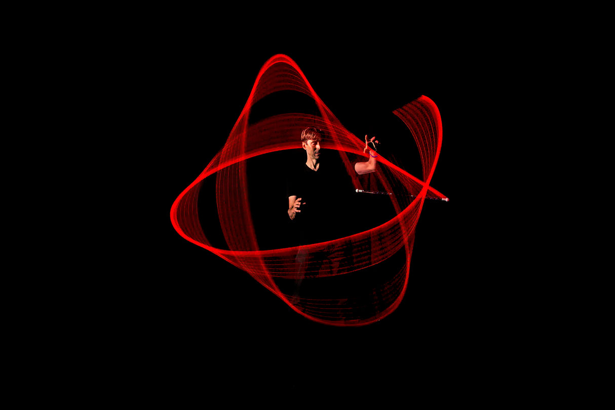 Person creating swirling red light patterns in darkness using Wandini Glow Wand LED wand.