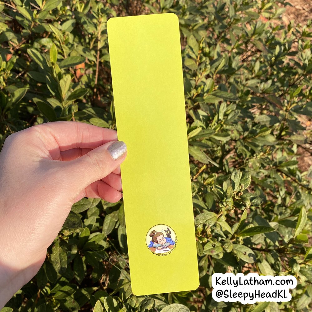 Dinosaur Clouds Bookmark showing solid bright yellow back with artist logo, held outdoors in natural light.