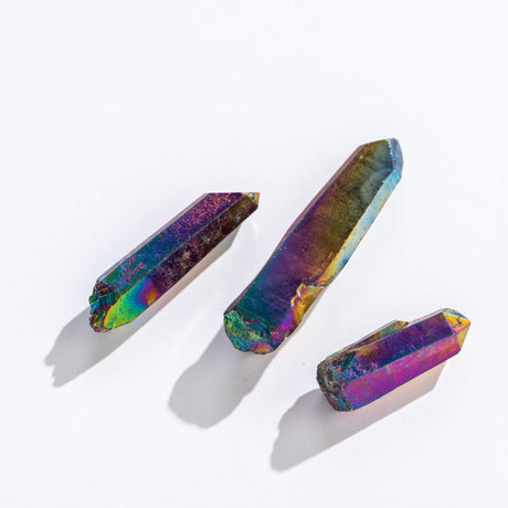 Crystal Point | Rainbow Aura showing three unique iridescent quartz points with vibrant rainbow colors on a white background.