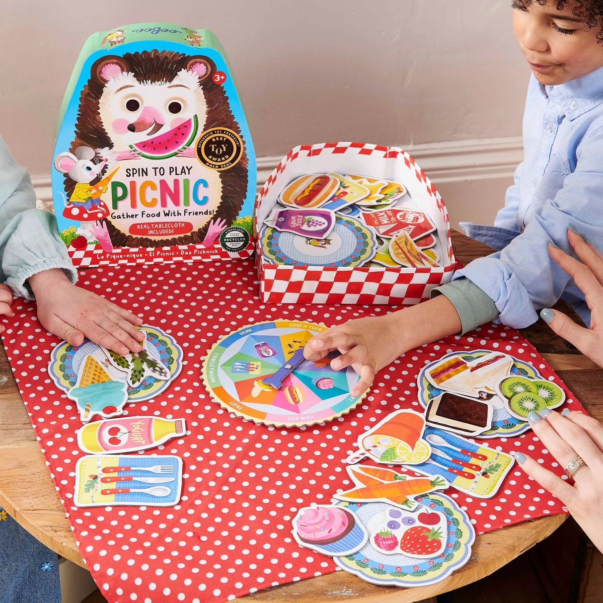 Picnic Spin to Play game with colorful spinner and food pieces on a red polka dot tablecloth, kids playing together.