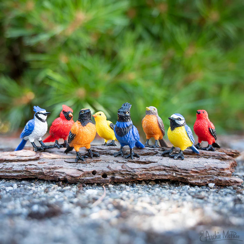 A Collection of Mini Garden Birds showing eight colorful vinyl bird figurines arranged on a piece of wood outdoors.