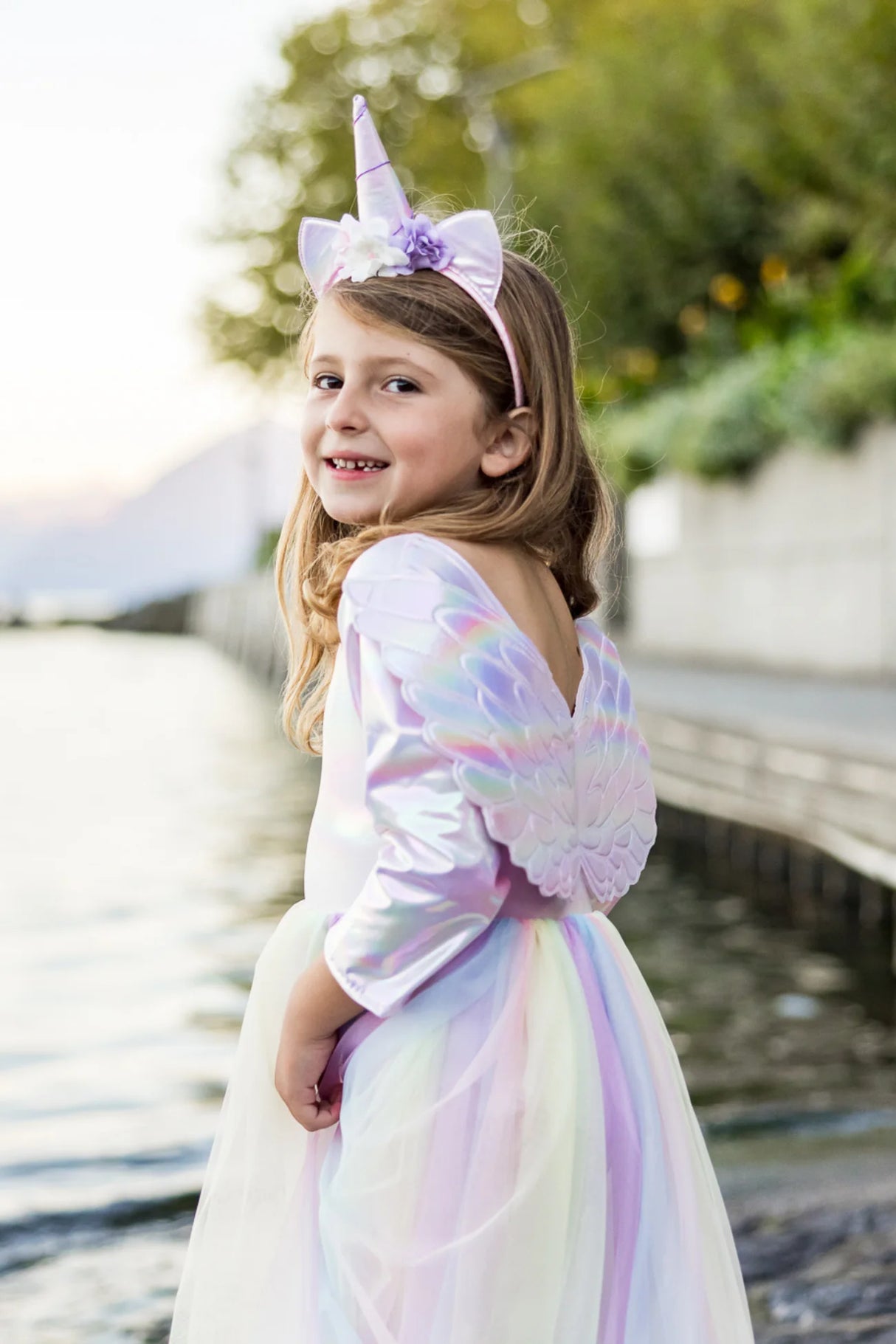 Young girl wearing Alicorn Dress & Wings & Headband with iridescent fabric and rainbow tulle skirt by the water.