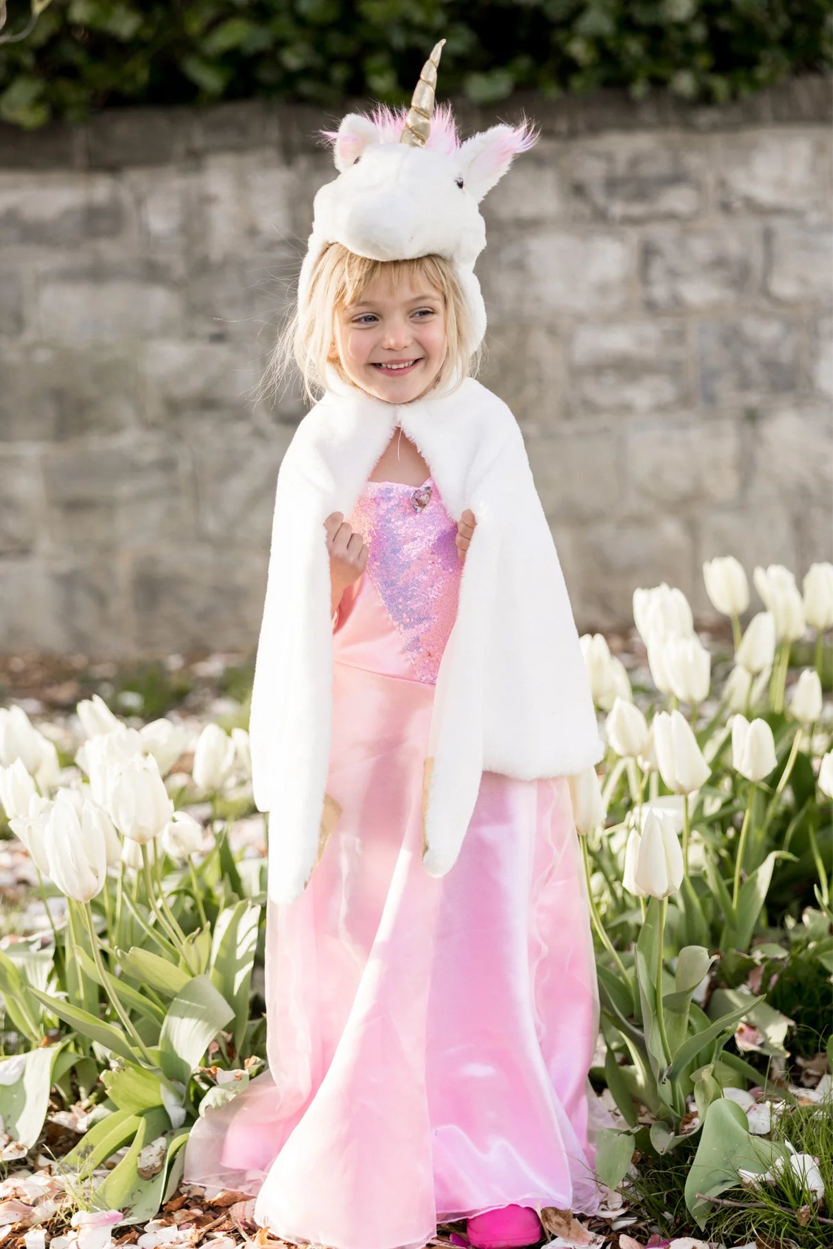 Young girl wearing the Unicorn Cuddle Cape | Size 4-6 with a soft white unicorn hood and pink dress outdoors.