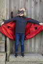 Child wearing Spider Bat Reversible Cape & Mask Size 4-6 showing red spider web satin interior with black spider details.